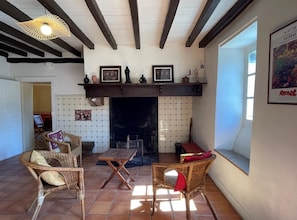 A cozy living room with a fireplace, wicker furniture, and a large window. - CHEZ CAZALETS - SUSMIOU (SUSMIOU)