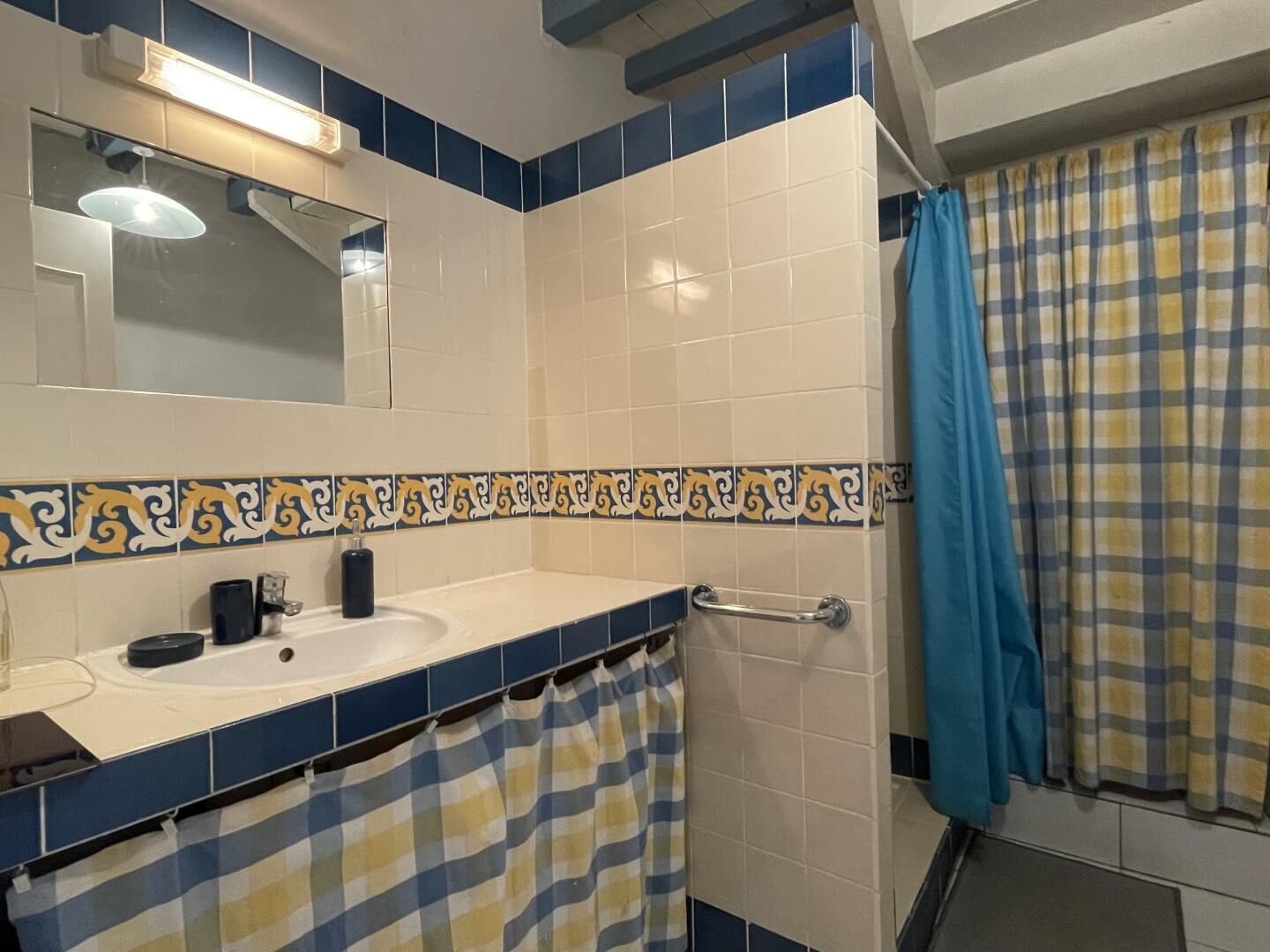 A bathroom with a white sink, blue and beige tiles, a mirror, and a blue shower curtain.