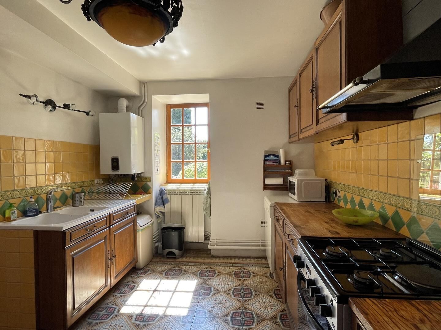 Eine Küche mit Herd, Spüle und Schränken. Ein Fenster sorgt für natürliches Licht.