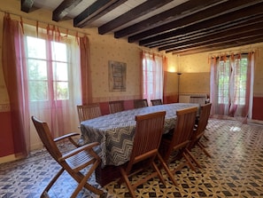A dining room with a large table, wooden chairs, patterned floor tiles, and large windows with curtains. - CHEZ CAZALETS - SUSMIOU (SUSMIOU)