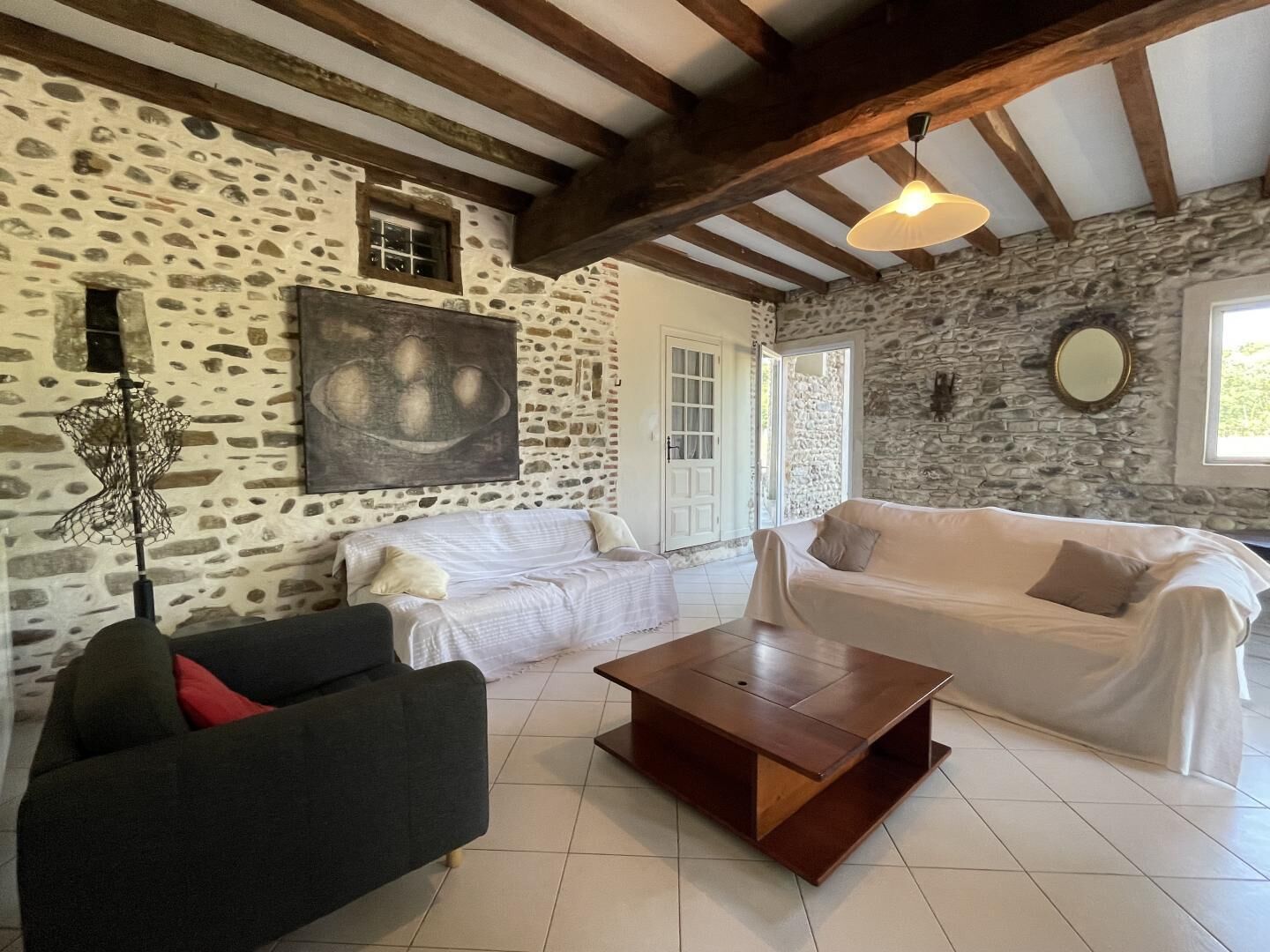 A cozy living room with stone walls, wooden beams, a large painting, and a modern coffee table.