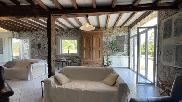A spacious living area with a covered sofa, a wooden cabinet, and a stone wall. - CHEZ CAZALETS - SUSMIOU (SUSMIOU)