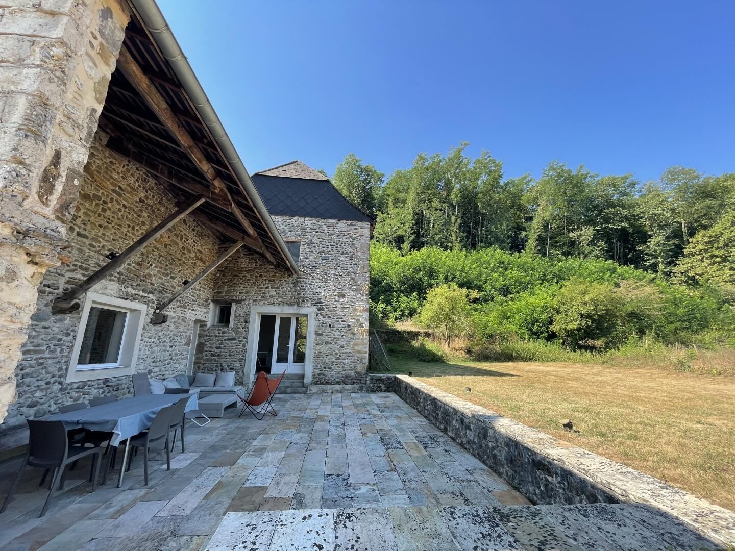 A stone building with a patio area, outdoor seating, and a view of a forested area.