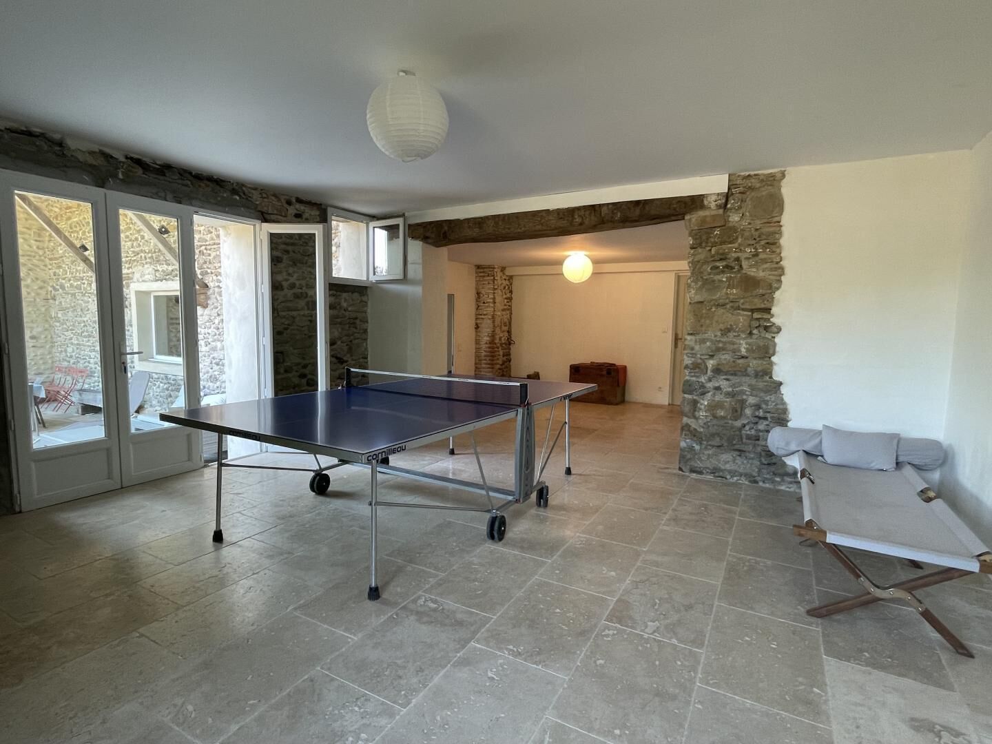 Habitació amb taula de ping-pong, parets de pedra i un llit amb dosser blanc.
