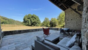 An outdoor patio with stone flooring, a wicker sofa, a red chair, and a table. - CHEZ CAZALETS - SUSMIOU (SUSMIOU)