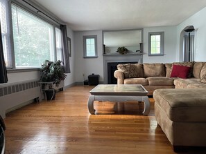 A living room with a beige sofa, a coffee table, a fireplace, and a large window with blinds.
