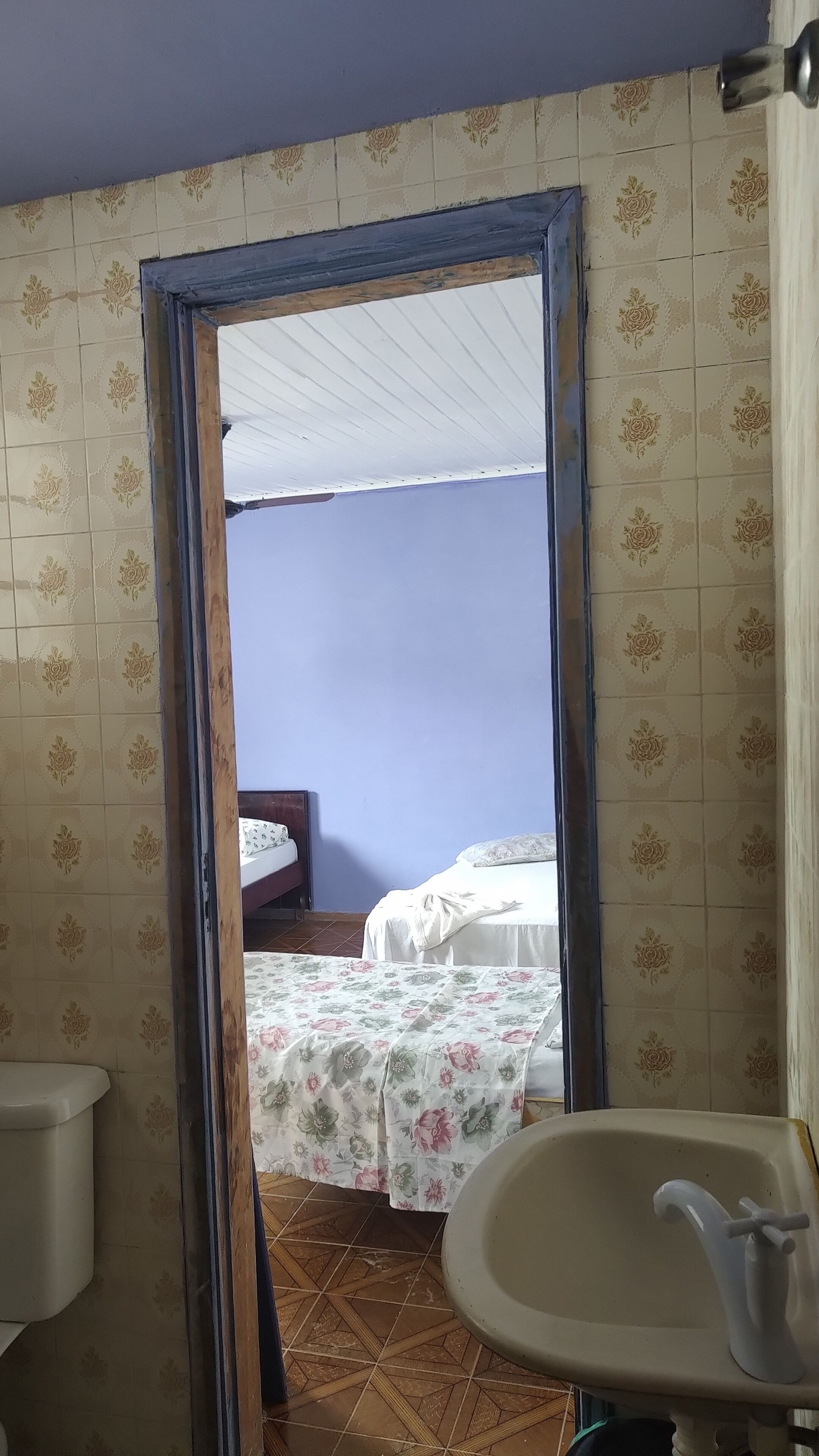 A bathroom with a sink and toilet, a bed with floral bedding, and a tiled floor.