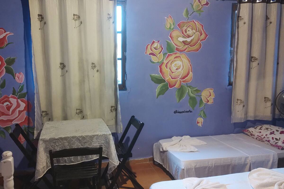 A room with a table and chairs, a bed with a white bedspread, and floral wall art.
