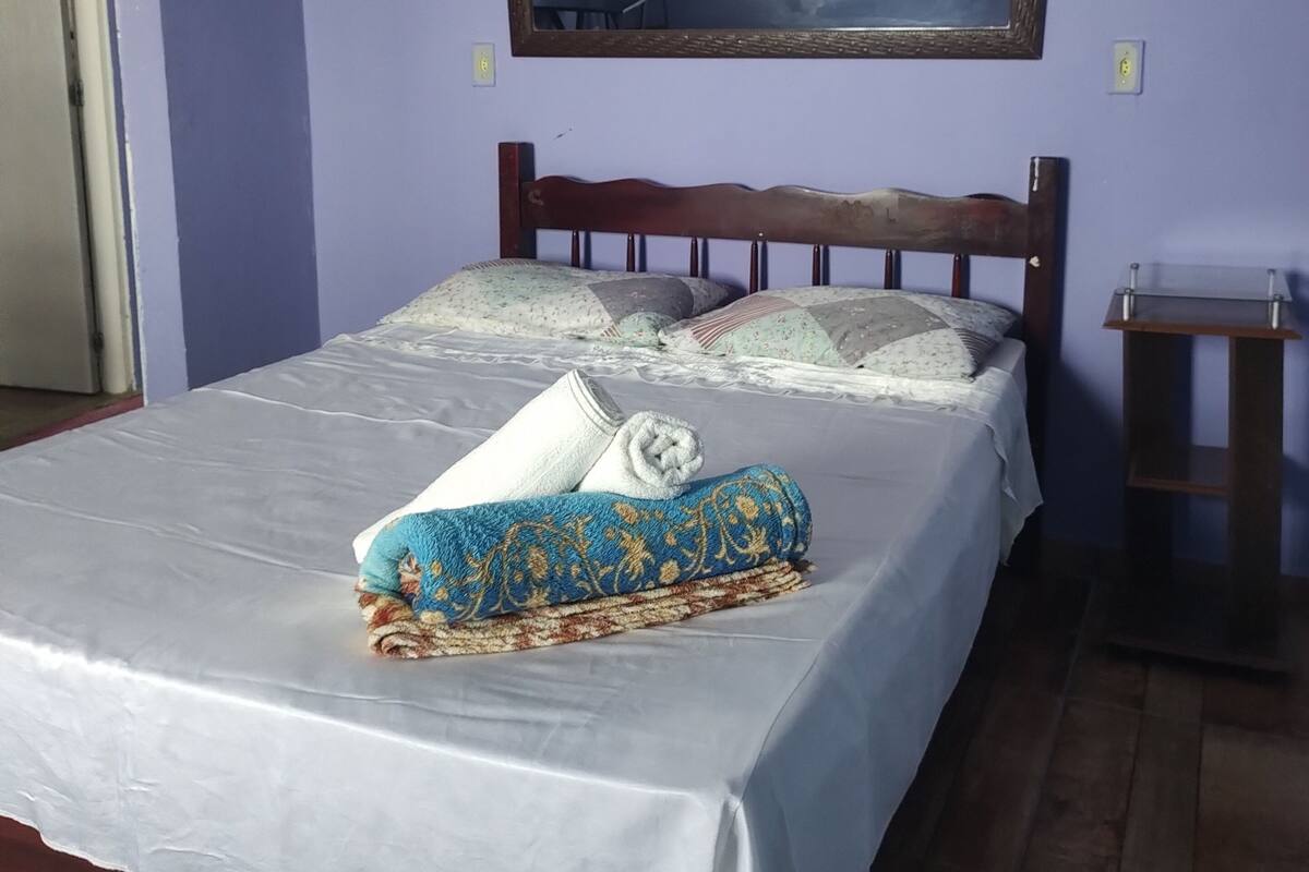 A bedroom with a bed, a wooden headboard, a mirror, and a bedside table.