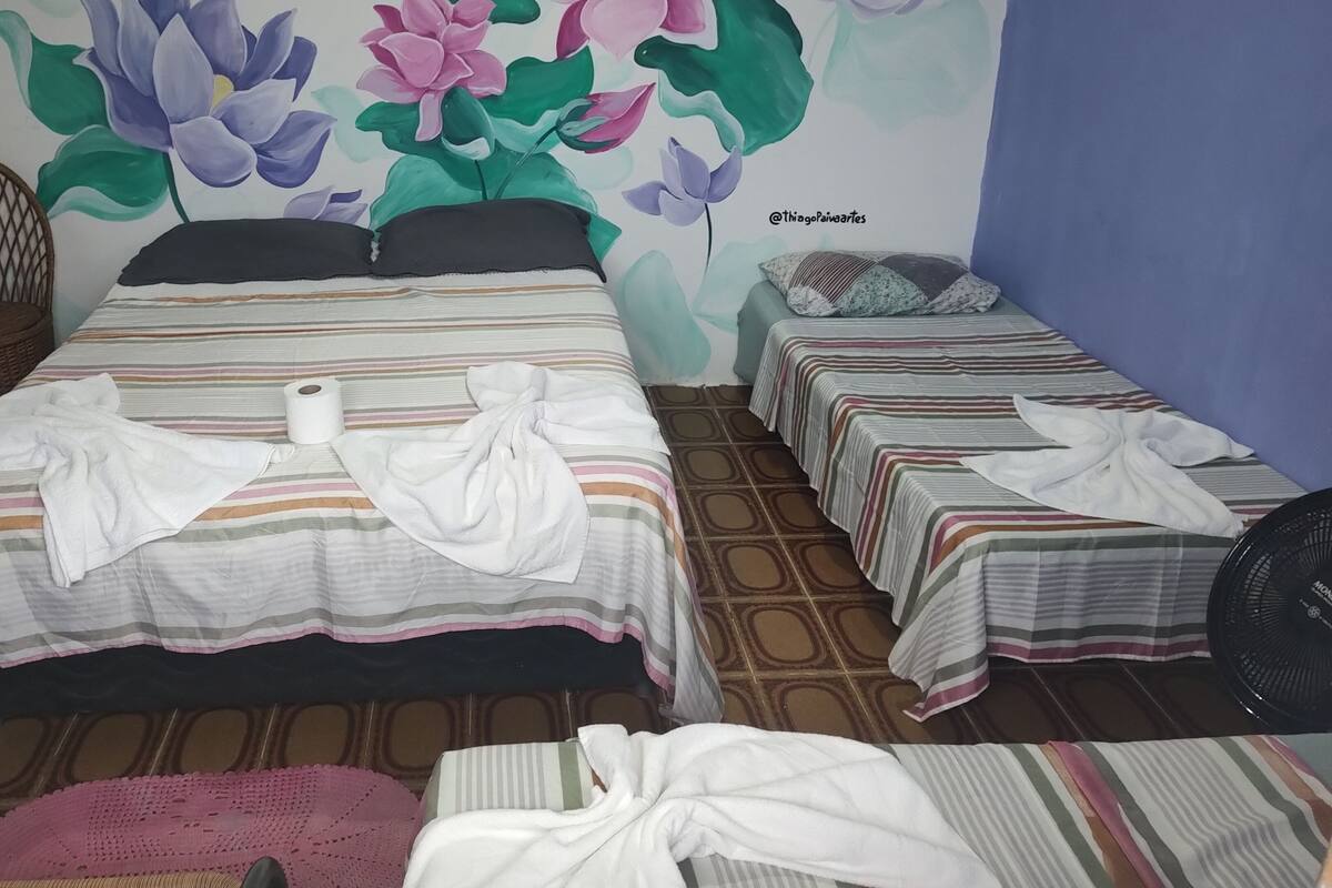 A room with two beds, a wicker chair, and a wall mural.