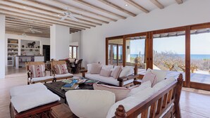 Ein großzügiger Wohnbereich mit Holzboden, einer Sofagarnitur, einem Couchtisch und Meerblick durch große Fenster.