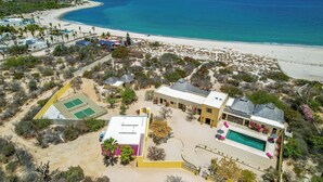 Ein Luftbild eines Küsteneigentums mit Swimmingpool, Tennisplätzen und Strand.