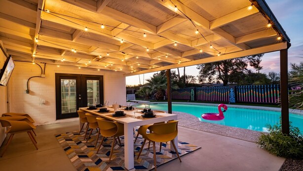 Un patio exterior con piscina, una mesa de comedor lista para seis personas y un flotador con forma de flamenco rosa.
