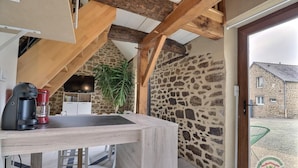 A rustic kitchen with a stone wall, wooden beams, a coffee machine, and a TV.