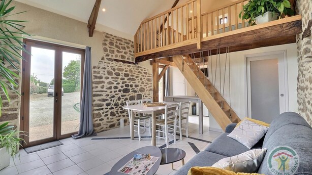 A spacious living area with a stone wall, a wooden staircase, a dining table, and a sofa.