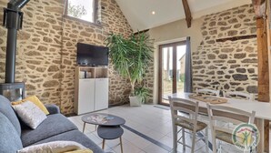 A cozy room with a stone wall, a flat-screen TV, a sofa, a dining table, and a potted plant.