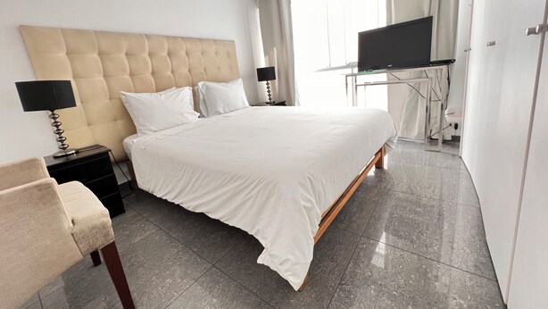 Una habitación de hotel moderna con una cama grande, un televisor sobre un mueble bajo, un escritorio con una silla y una ventana con cortinas.