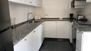 Cocina compacta con armarios blancos, encimera de granito, un lavabo, microondas y tostadora.