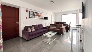 Una sala de estar moderna con un sofá púrpura, una mesa de centro de vidrio y una zona de comedor con sillas.