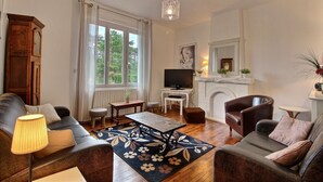 A living room with a fireplace, a television, a sofa, a coffee table, and a lamp. - Les Magnolias - Frehel (FREHEL)