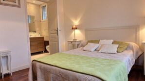 A bedroom with a bed, bedside tables, a nightstand, a lamp, and a bathroom visible through an open door. - Les Magnolias - Frehel (FREHEL)