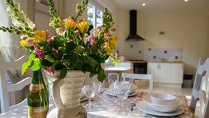 A dining table set with a vase of flowers, a bottle of wine, and empty dinnerware. - Les Magnolias - Frehel (FREHEL)