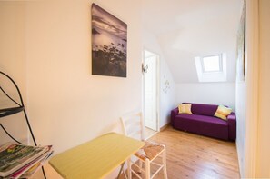 Et lille, lyst rum med trægulv, en lilla sofa, en hvid stol og et lille bord.