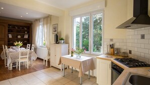 A kitchen with a dining area, featuring a stove, sink, and a window with a view of greenery. - Les Magnolias - Frehel (FREHEL)