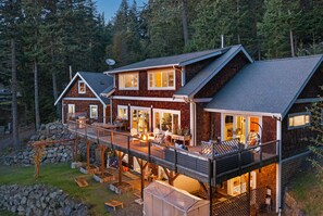 Une grande maison à plusieurs étages, dotée d’une terrasse et d’un espace salon extérieur, entourée d’une forêt.