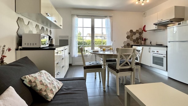A compact kitchen with a dining area, a sofa, and a window with curtains.