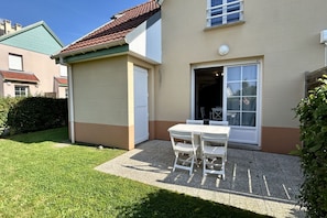 Una casa con un patio, un tavolo e sedie bianche e una porta che dà su una stanza.