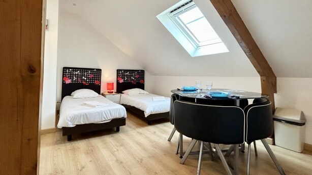 A small, cozy room with two beds, a round table with chairs, a skylight, and a wooden ceiling beam. - Studio for 2 in the city center (Le Crotoy)