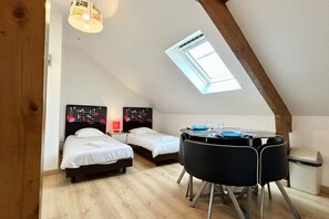 A small, cozy room with two beds, a round table with chairs, a skylight, and a wooden ceiling beam. - Studio for 2 in the city center (Le Crotoy)