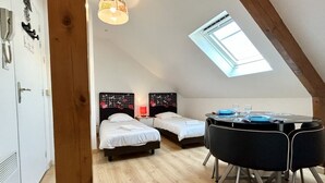 A room with two beds, a table with chairs, a skylight, and a wooden ceiling beam. - Studio for 2 in the city center (Le Crotoy)