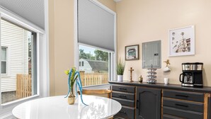 Une cuisine avec une table blanche, des meubles de couleur sombre et une fenêtre avec des stores.