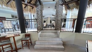 Eine Hotelhalle mit Treppe, Holzmöbeln und einem Strohdach.