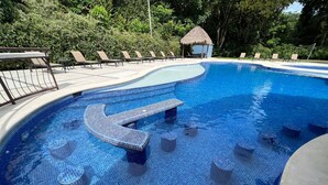 Ein Schwimmbad mit einem einzigartigen Fliesenmuster, Liegestühlen und einer kleinen Hütte in einer üppigen, grünen Umgebung.