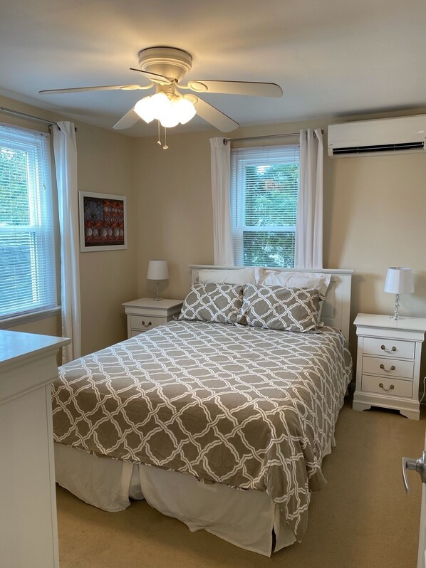 Quarto com cama, duas mesas de cabeceira, ventoinha no teto e janela com persianas.