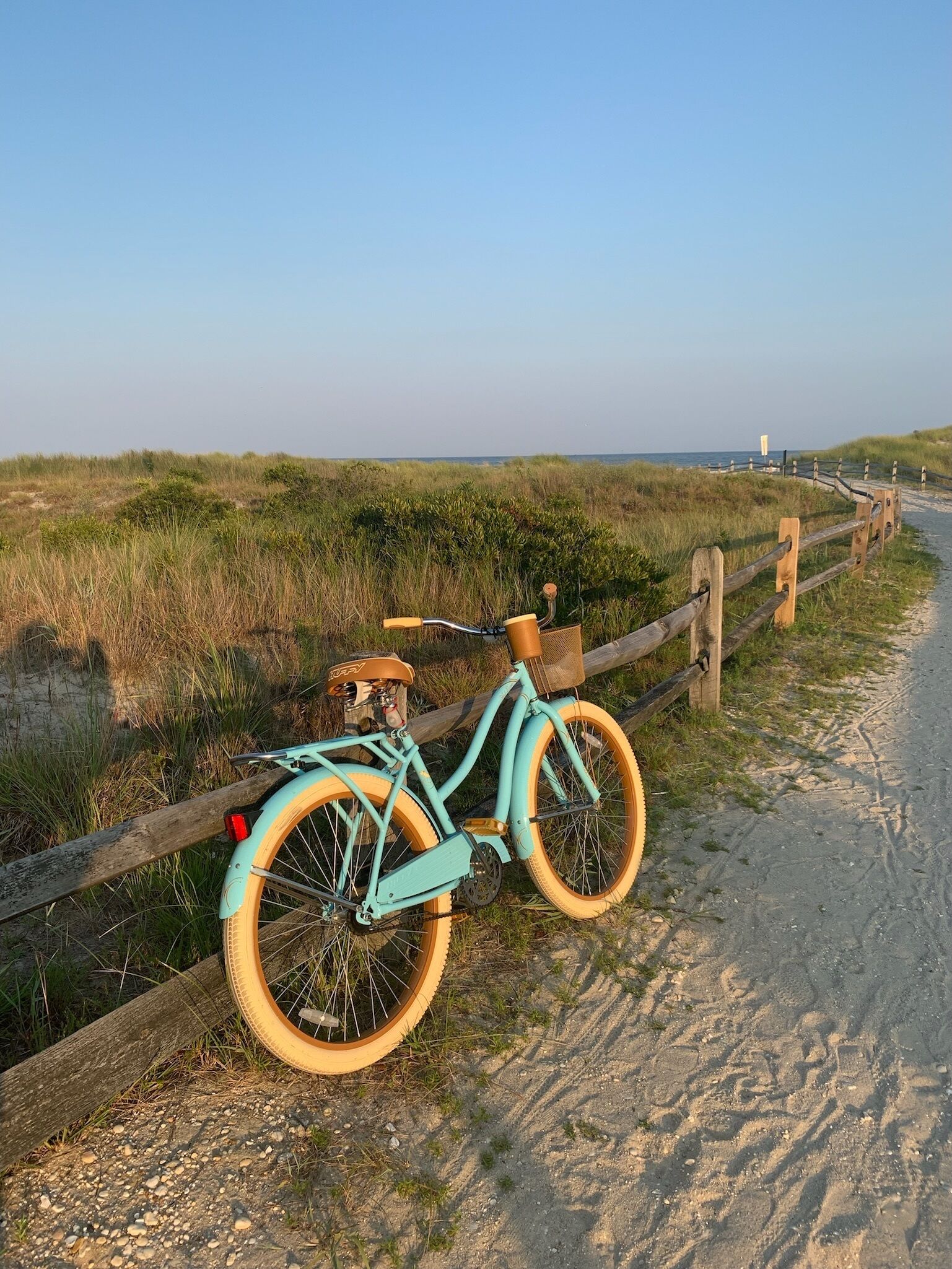 A turquoise bicycle parked on a sandy path beside a wooden fence.