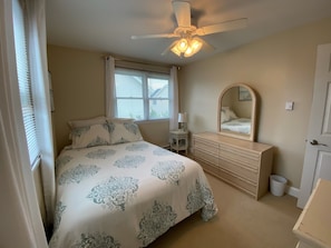 A bedroom with a bed, a dresser, a mirror, and a ceiling fan.