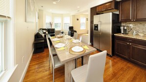 Une cuisine moderne avec des meubles en bois, un réfrigérateur en acier inoxydable et un coin repas doté d’une longue table dressée pour six personnes.