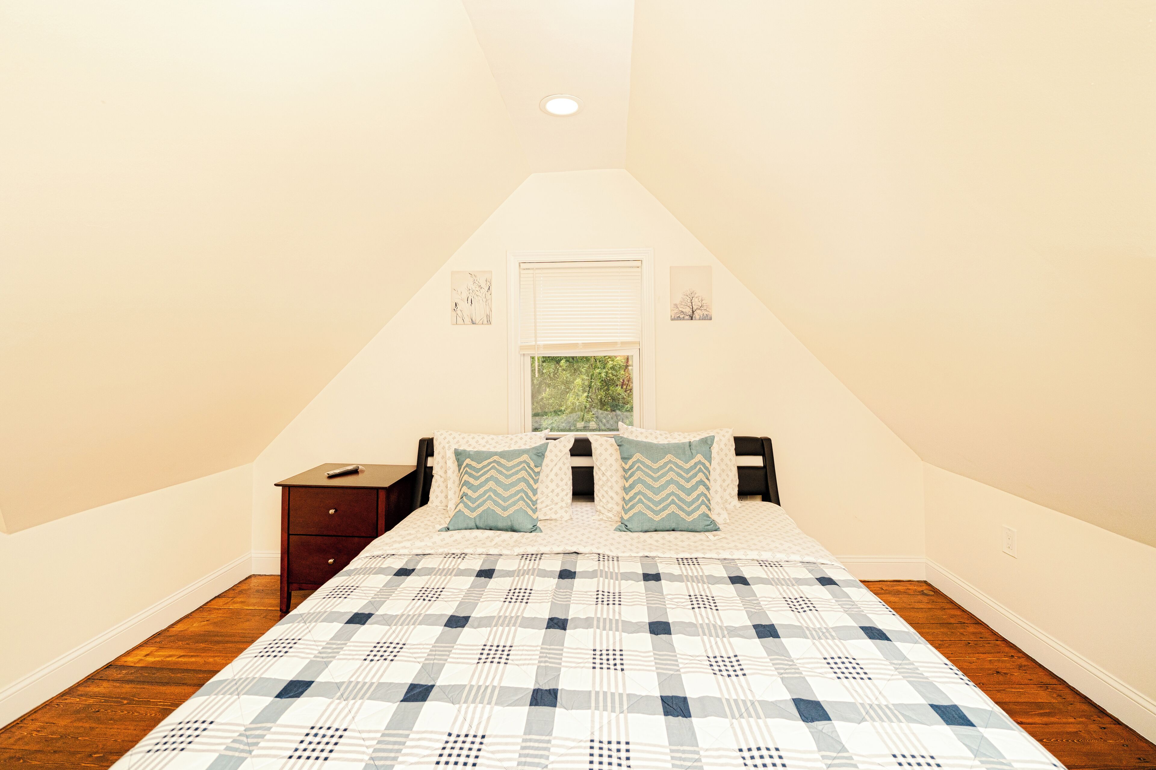 Ein Schlafzimmer mit Bett, Nachttisch, Fenster und Deckenleuchte.