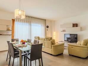 A modern living room with a dining area, a sofa set, a TV, and a large window with curtains. - Casa Tondi by Interhome (Porlezza)
