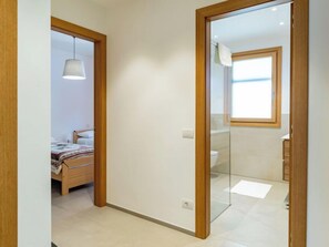 Um corredor com uma porta de madeira que dá para um quarto com cama e luminária pendente.