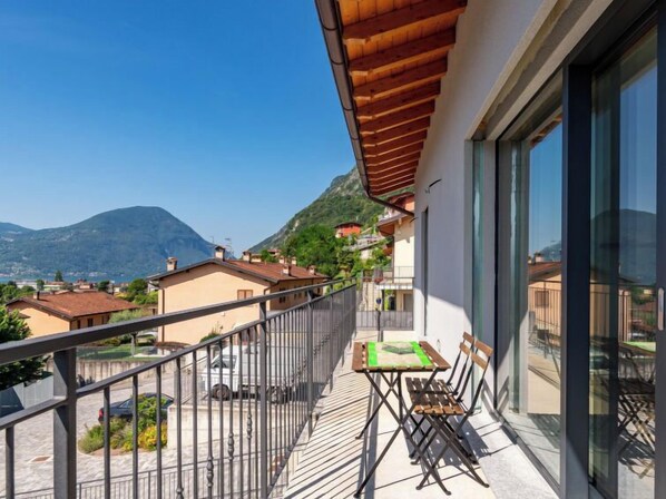 Varanda com mesa e cadeiras, vista para uma paisagem montanhosa com edifícios.