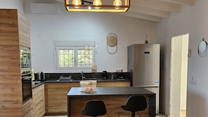 Une cuisine moderne avec des meubles en bois, un îlot central doté de tabourets, un four encastré et une fenêtre laissant entrer la lumière naturelle.