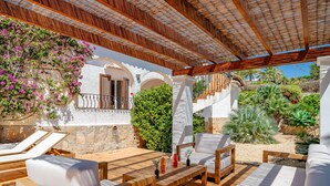 An outdoor patio with wooden furniture, a white wall with arches, and a variety of plants.