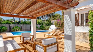 A covered outdoor area with a pool, lounge chairs, and a pergola.