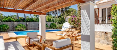 A covered outdoor area with a pool, lounge chairs, and a pergola.