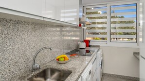 Une cuisine moderne dotée de plans de travail en granit, d’un évier en acier inoxydable, d’un four encastré et d’une fenêtre avec des stores.